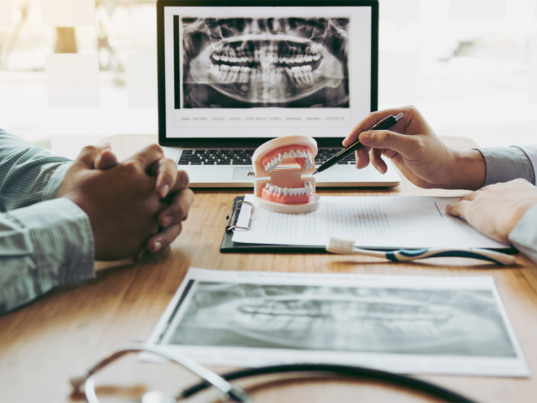 image of a person pointing at 3d model of teeth with xray in the background